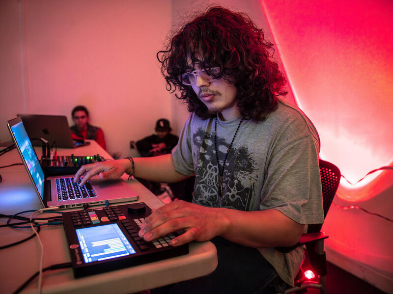 A photo of a man sittin at a table with a laptop and a soundboard. 
