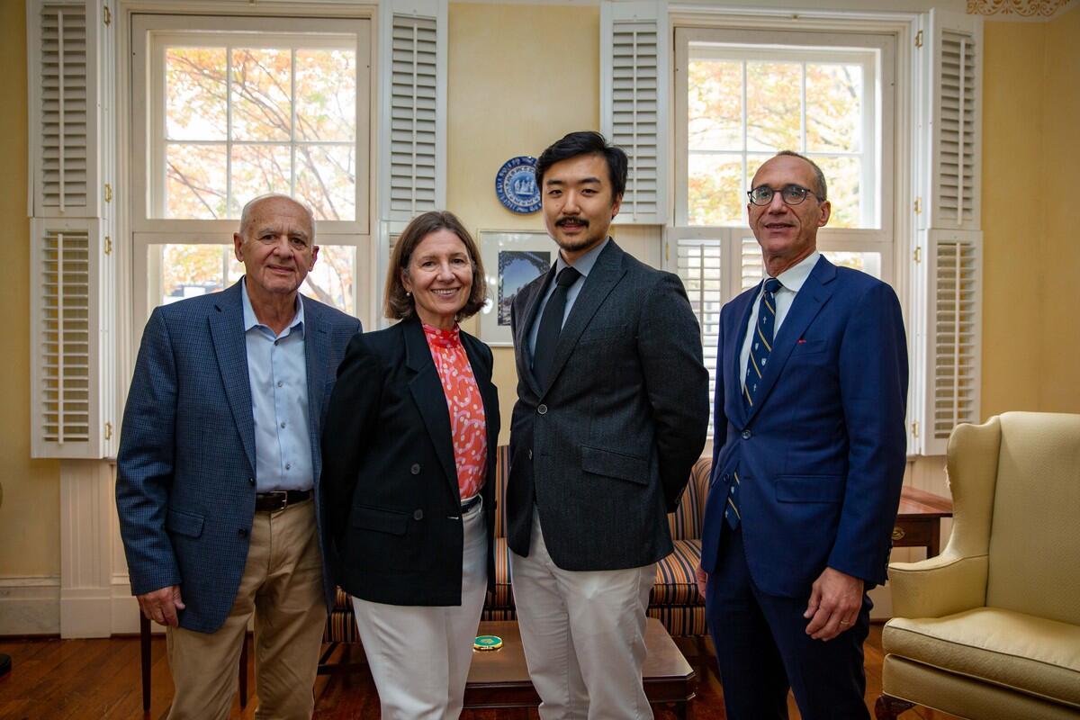 Four people standing next to each other in front of two windows. 