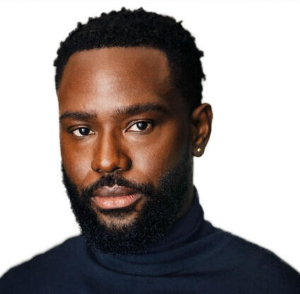 A photo of a man from the shoulders up. He has a beard and is wearing a black turtle neck shirt.