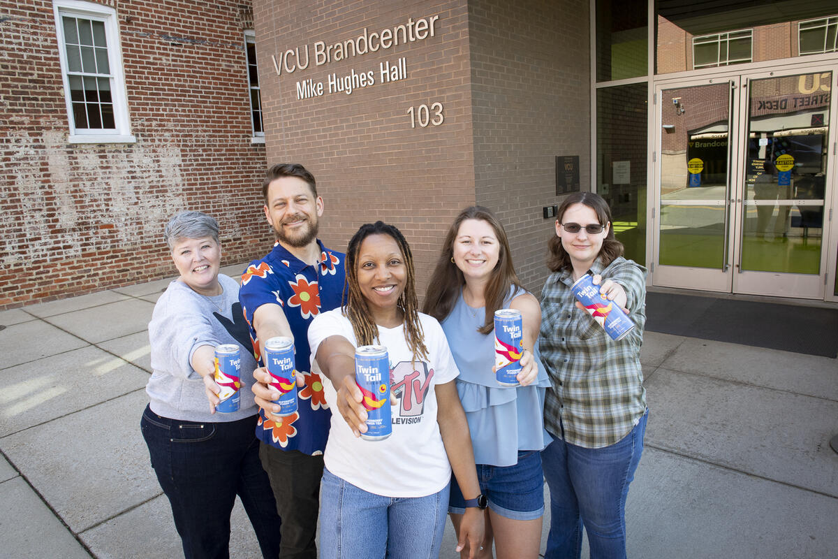 Five people each hold up a drink can to the camera.