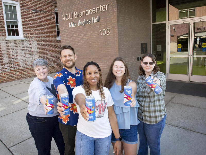 Five people each hold up a drink can to the camera.