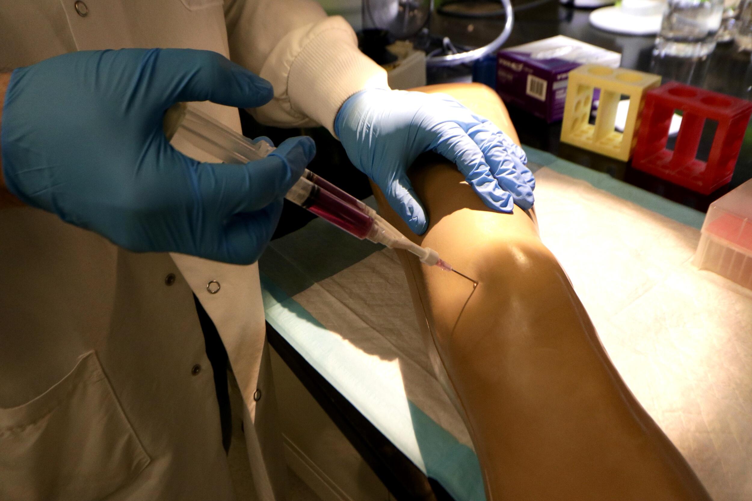A photo of two hands sticking a needle into a knee. 
