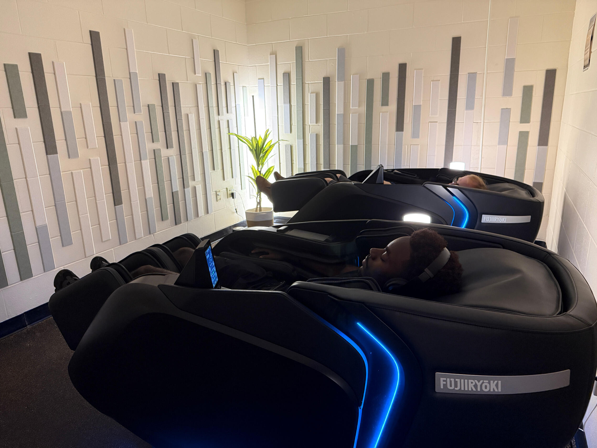 Two people lie down on black massage chairs.