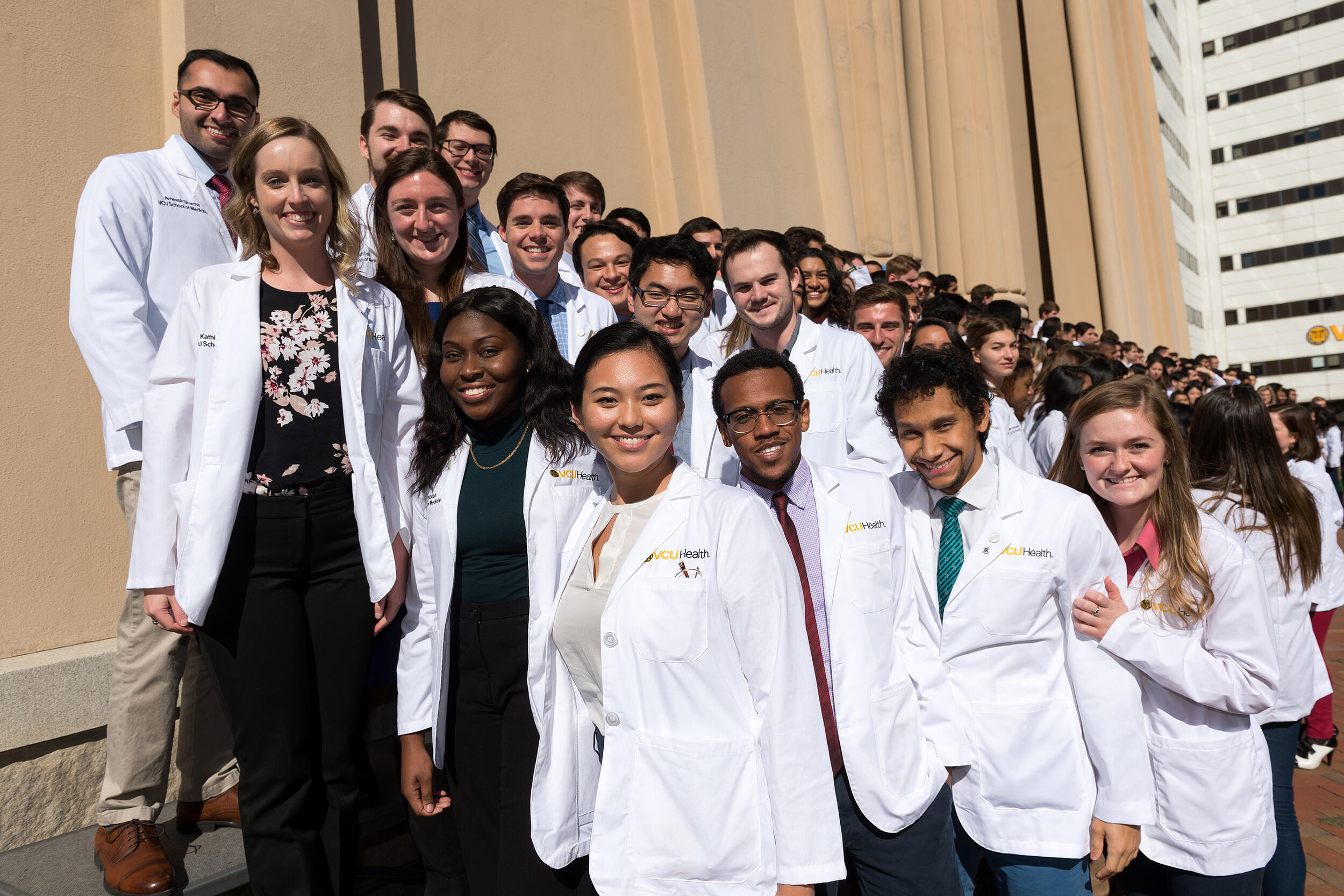 A group of students in white coats standing on stairs. 