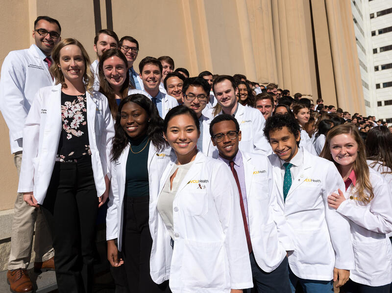 A group of students in white coats standing on stairs. 