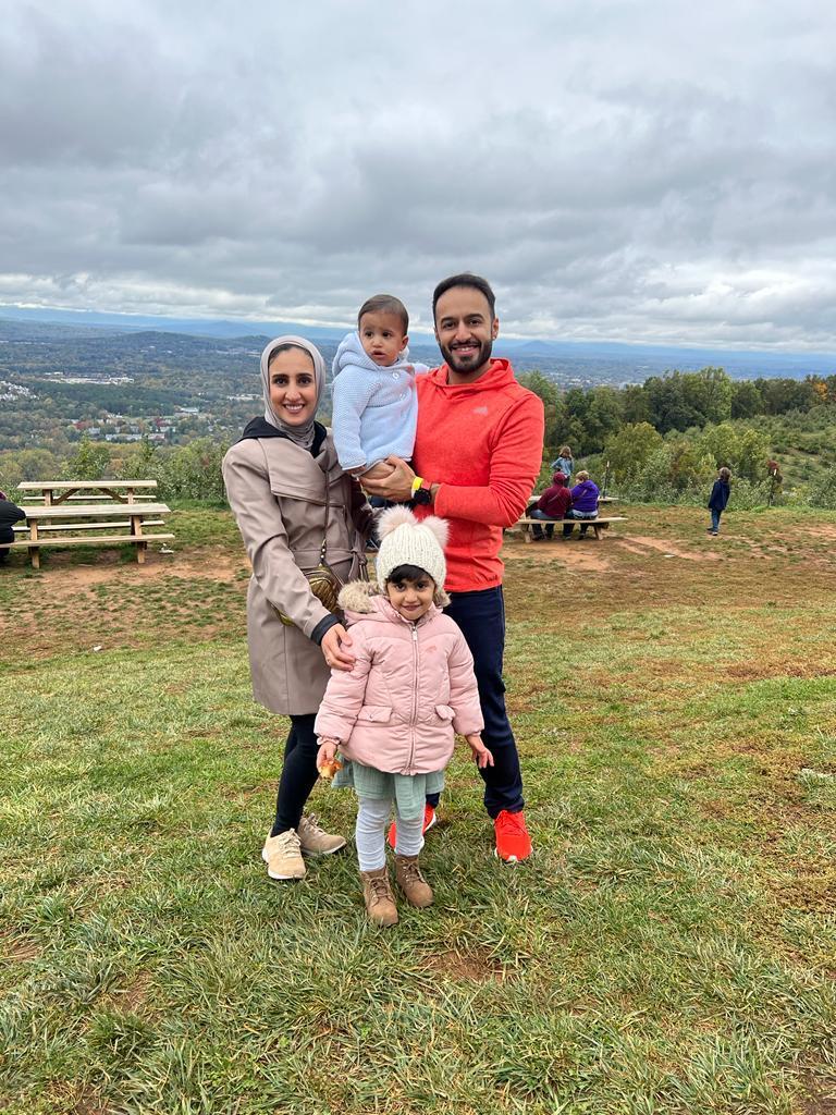 Abdullah Alawadhi, right, his wife Sarah Alkanderi, left, and their children standing between them in a crass field overlooking rolling hills. 