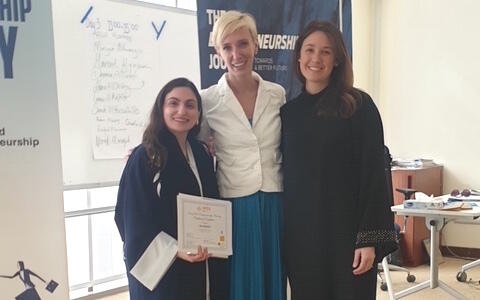 Three women stand together, one holding a certificate. 