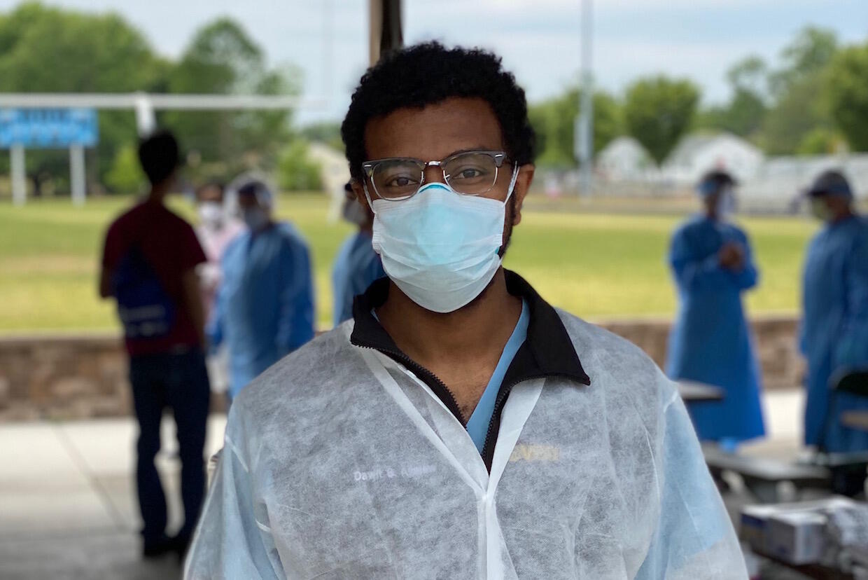 A person wearing a pair of glasses, a mask and medical scrubs.