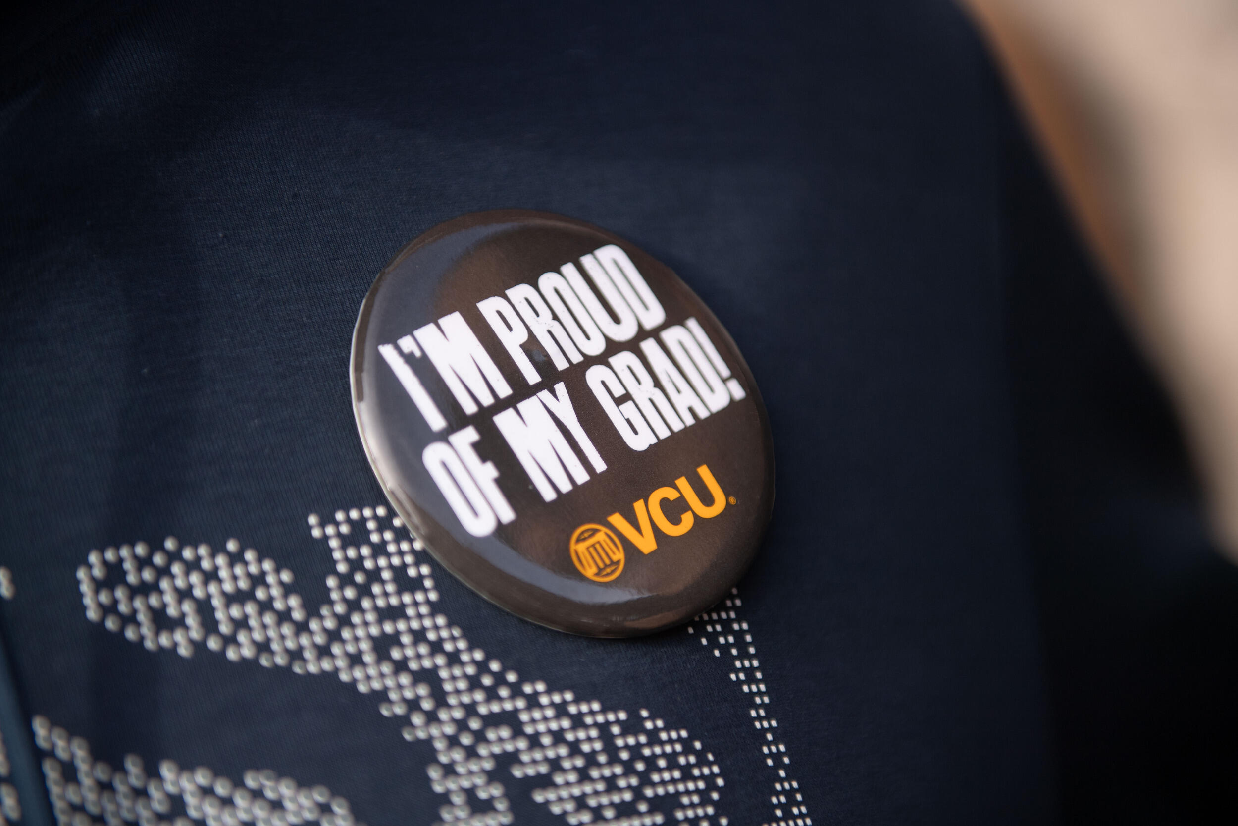 Button on shirt saying \"I'm proud of my grad!\" with a VCU logo.