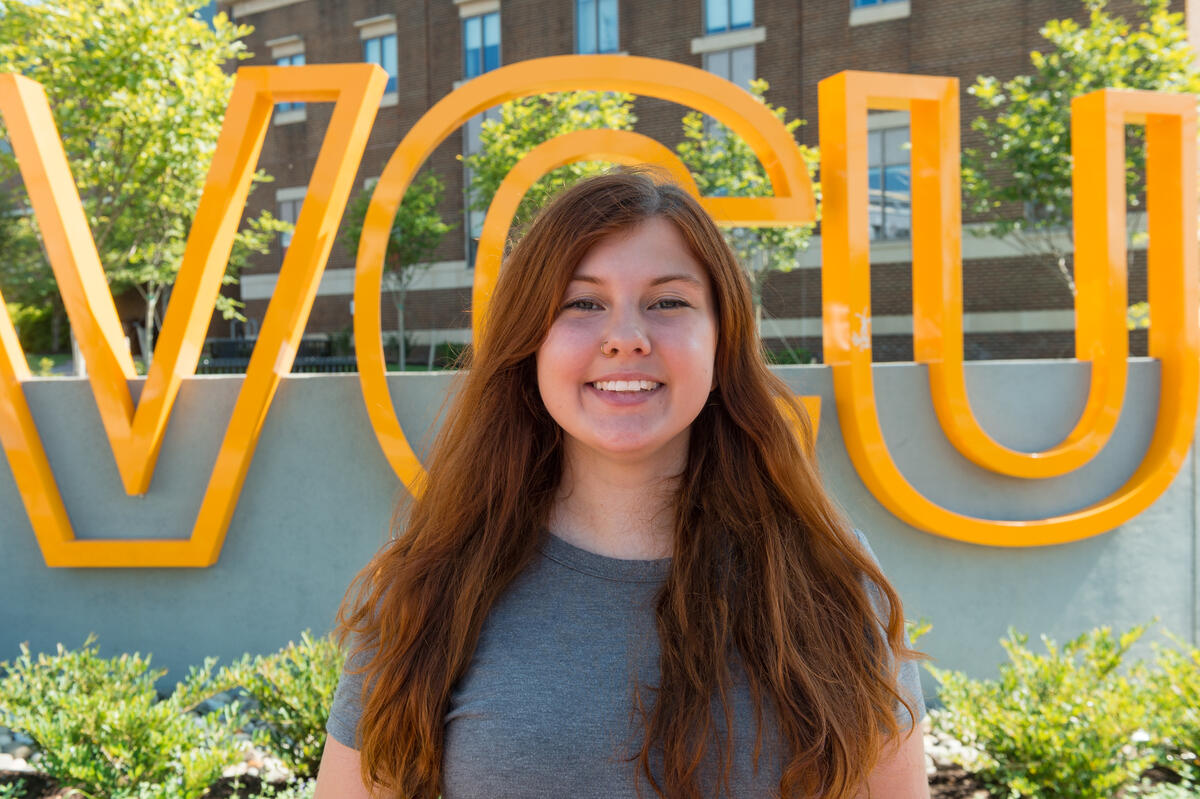 A portrait of Murell Sanders standing in front of a sign that says \"V C U\"