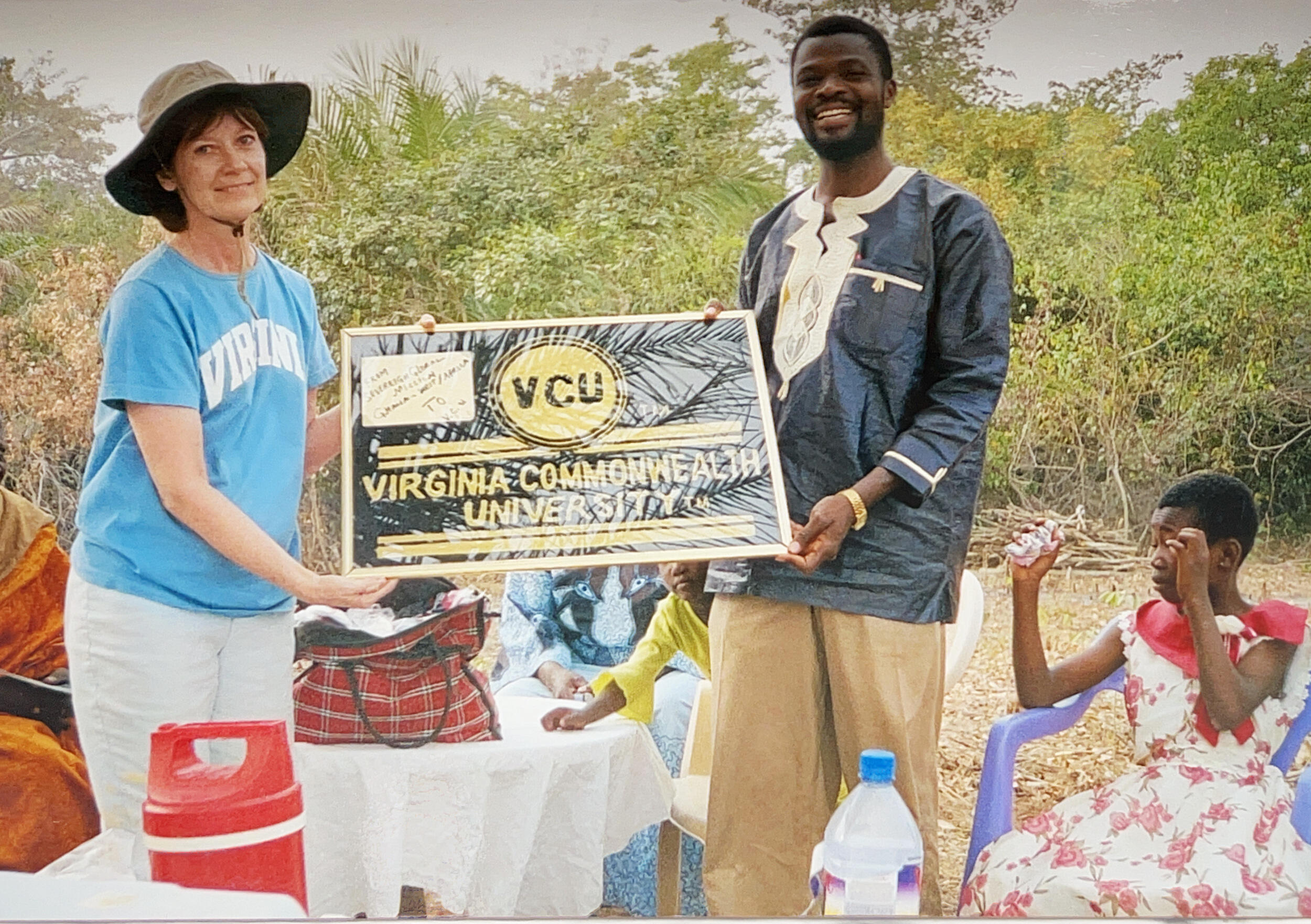 A photo of a man and a woman holding a black and yellow sign that reads \"VIRGINIA COMMONWEALTH UNIVERSITY.\" Next to the man is a child sitting in a chair. 
