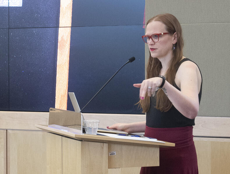 A photo of a woman standing a a podium and speaking. 