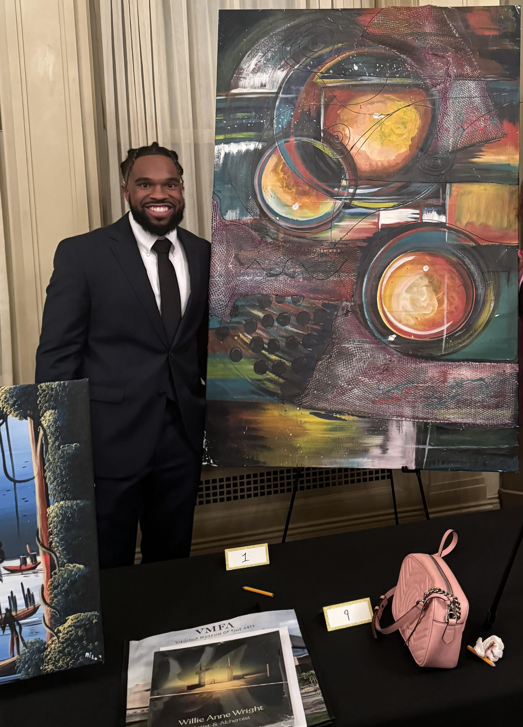 A photo of a man wearing a suit standing next to an abstract painting. 