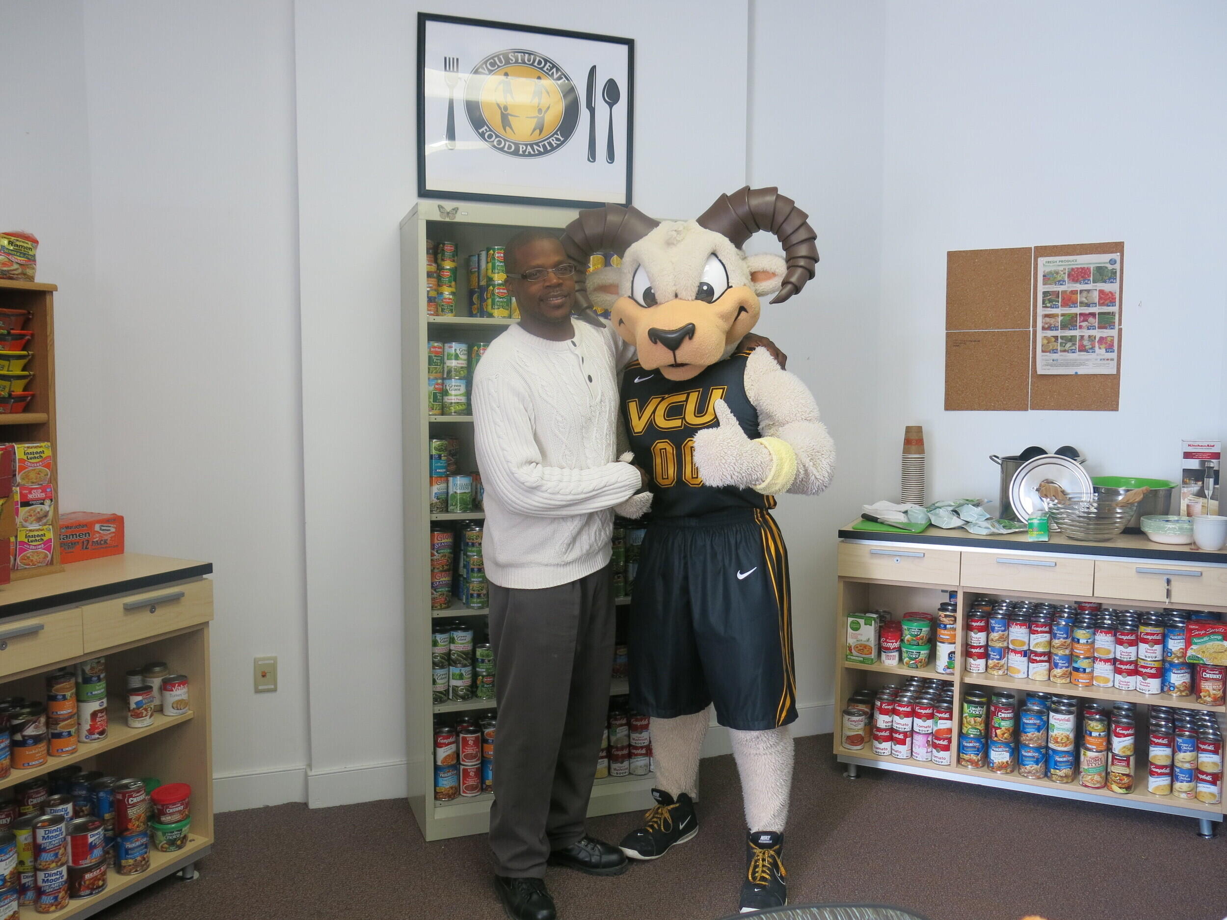 A man standing next to a Rodney the Ram mascot in a room filled with food on shelves. 