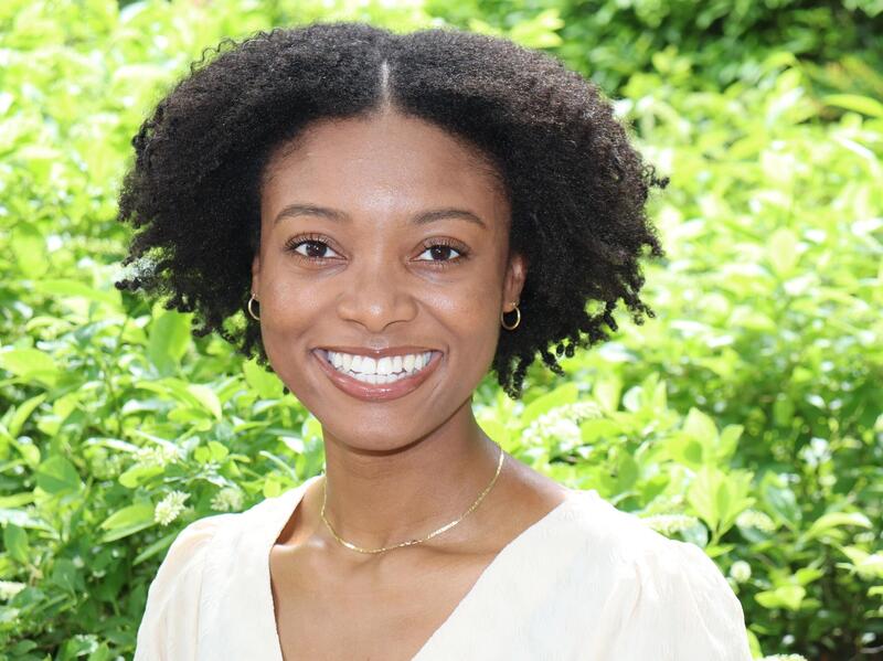 A woman smiling in front of foliage 