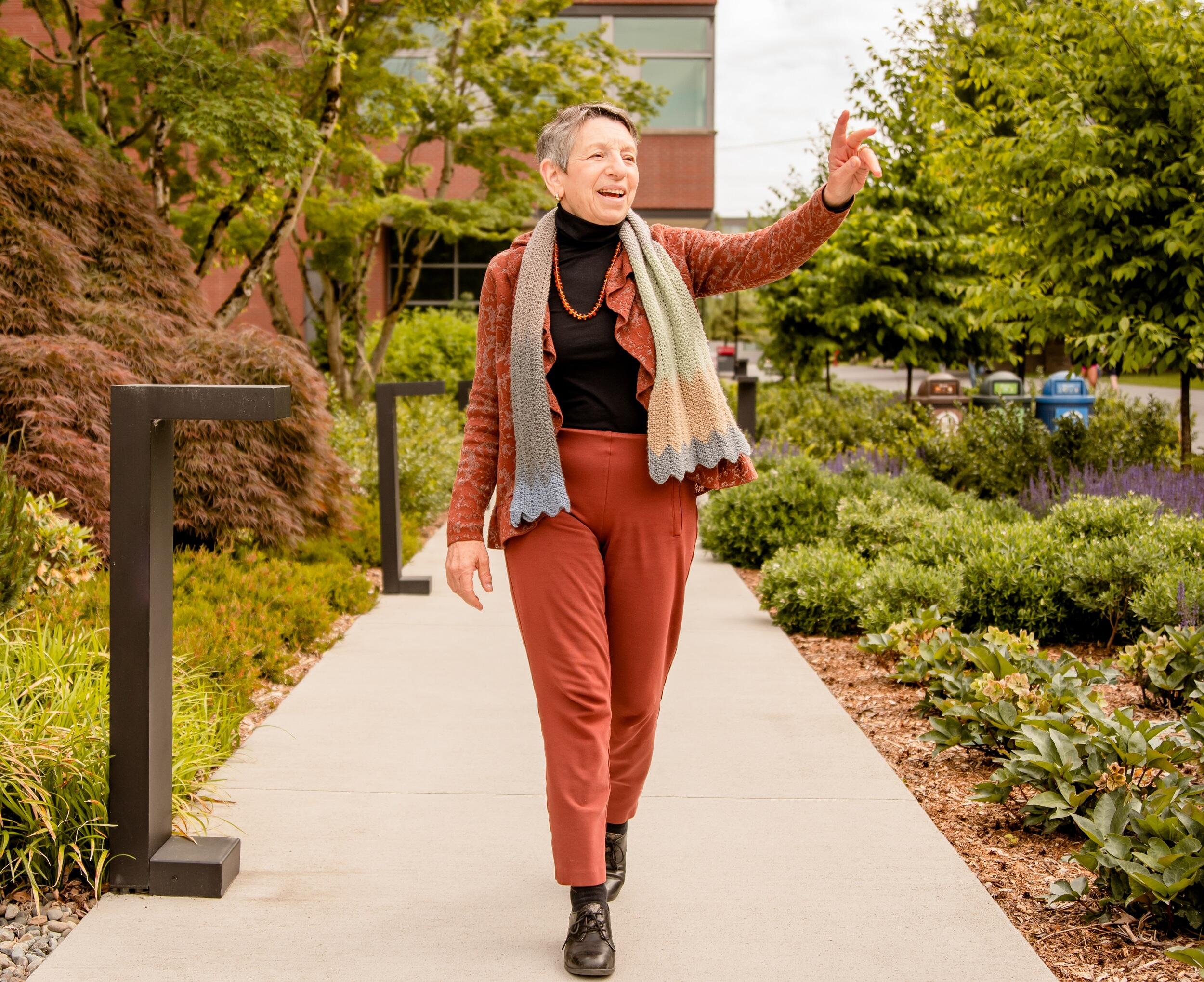 A woman walking down a path with her right arm raised. 