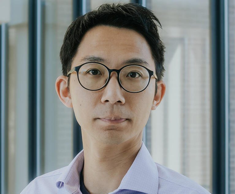 A photo of a man from the shoulders up. He is wearing glasses and a light blue collared shirt.
