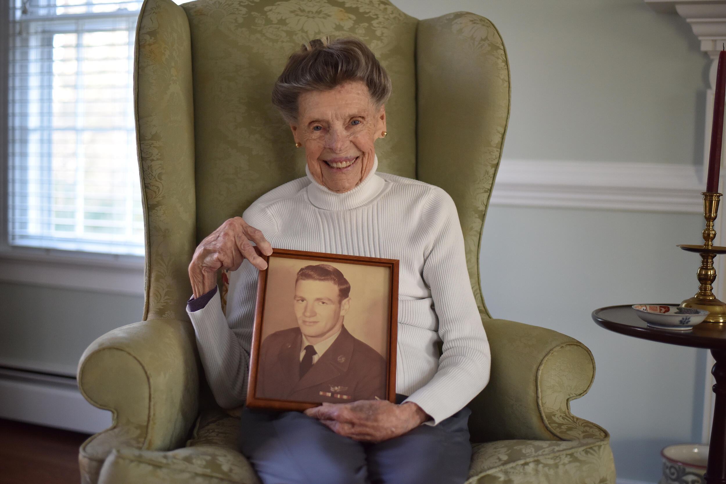 A photo of an old woman in a chair holding a sepia tone photo of a man in a military uniform. 