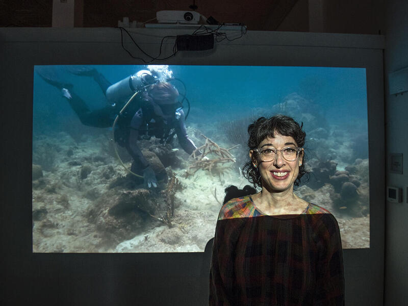 Woman standing in front of a projected image of an ocean scene.