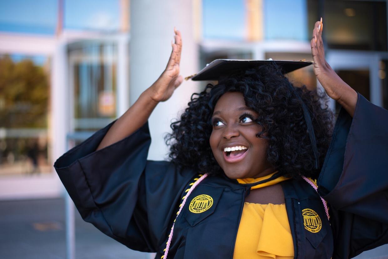 young V C U student standing in cap and gown outside the university library