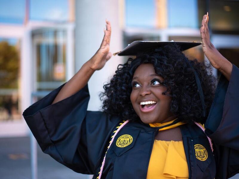 young V C U student standing in cap and gown outside the university library