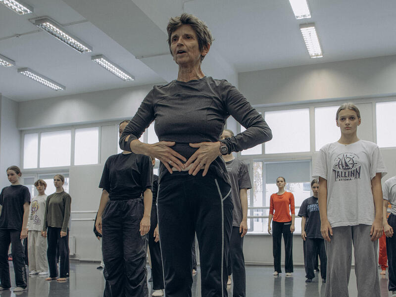 A photo of a woman standing in the front of a dance studio. Behind her several other people are standing