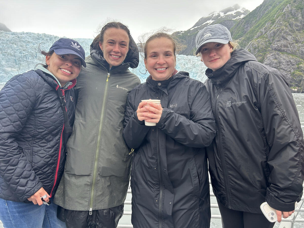 A group photo of five people wearing coats standing outside in front of snow and mountain tops. 
