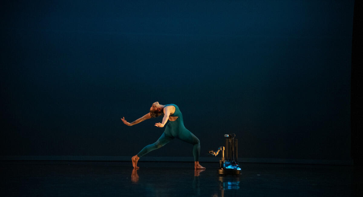 A woman dancing next to a robot. 