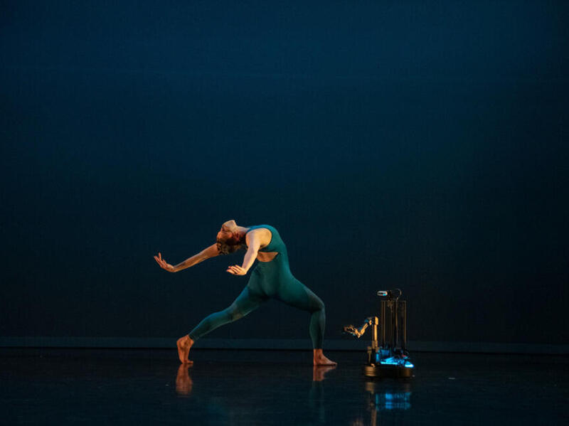 A woman dancing next to a robot. 