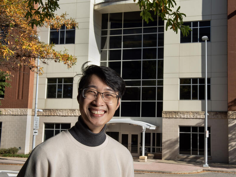 A smiling man in glasses stands in front of a large building.