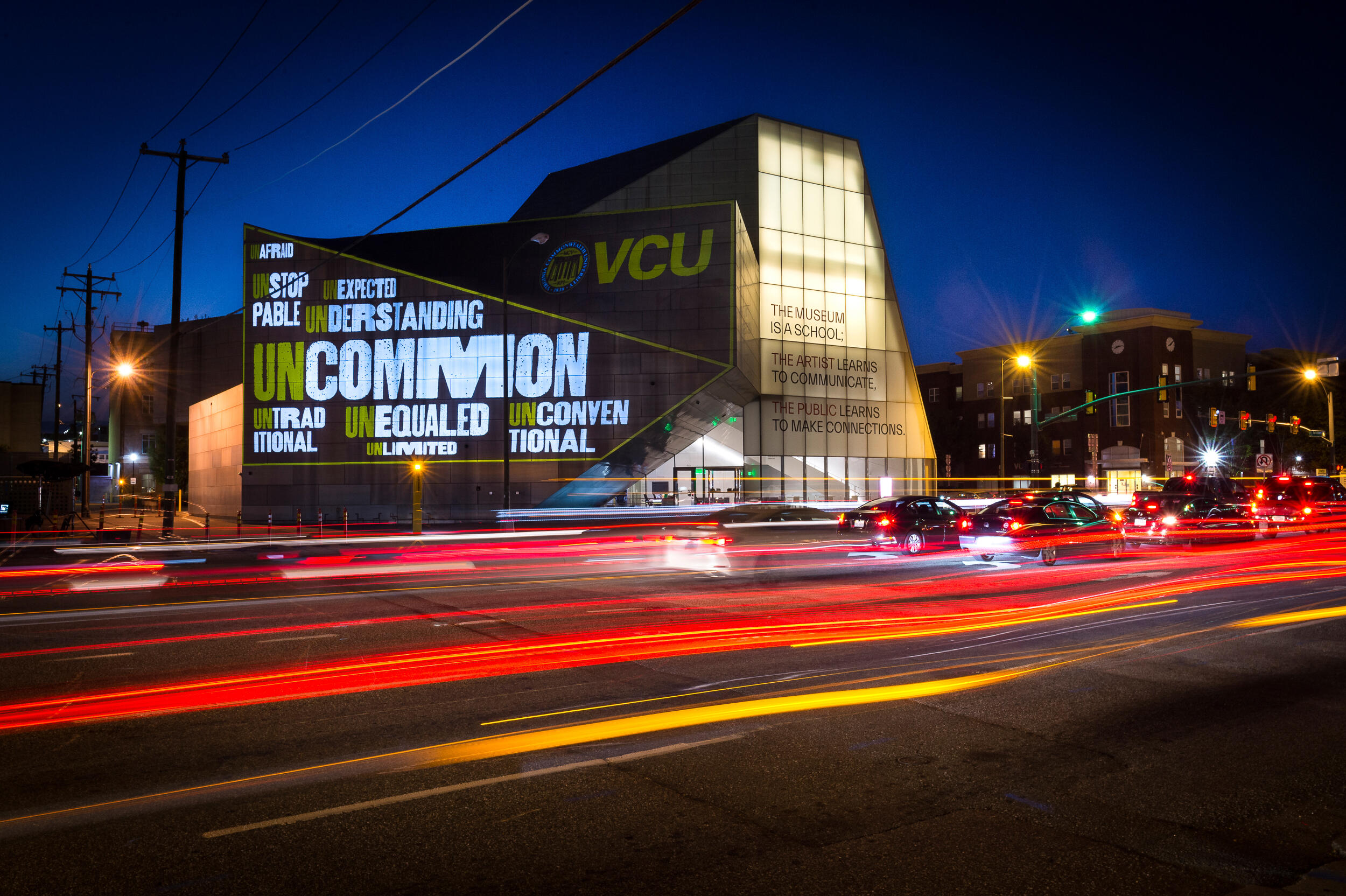 A long exposure image of cars passing by the Institute for Contemporary Art at VCU lit with a projection of an artistic rendering of a word cloud of words that represent the uncommon experience VCU offers: Unafraid, unlimited, understanding, unequaled, uncommon, unexpected, unstoppable and unconventional.