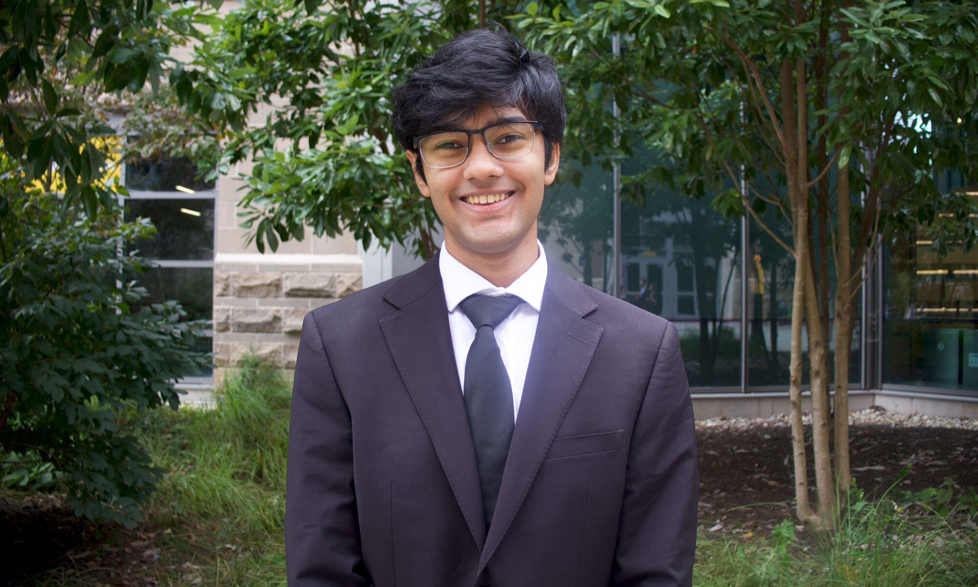 A photo of a man from the chest up. He is wering a black suit and tie, and a white button down shirt. 