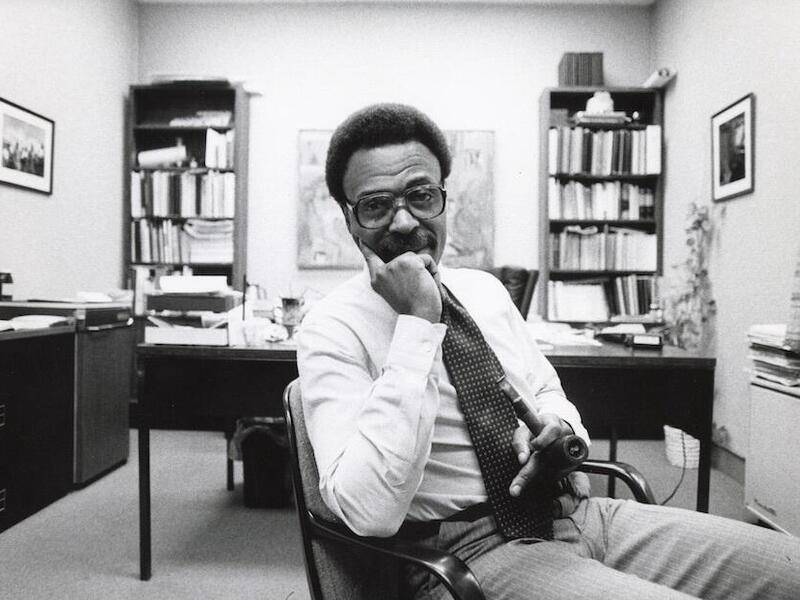 Murry DePillars seated inside an office holding a tobacco pipe.