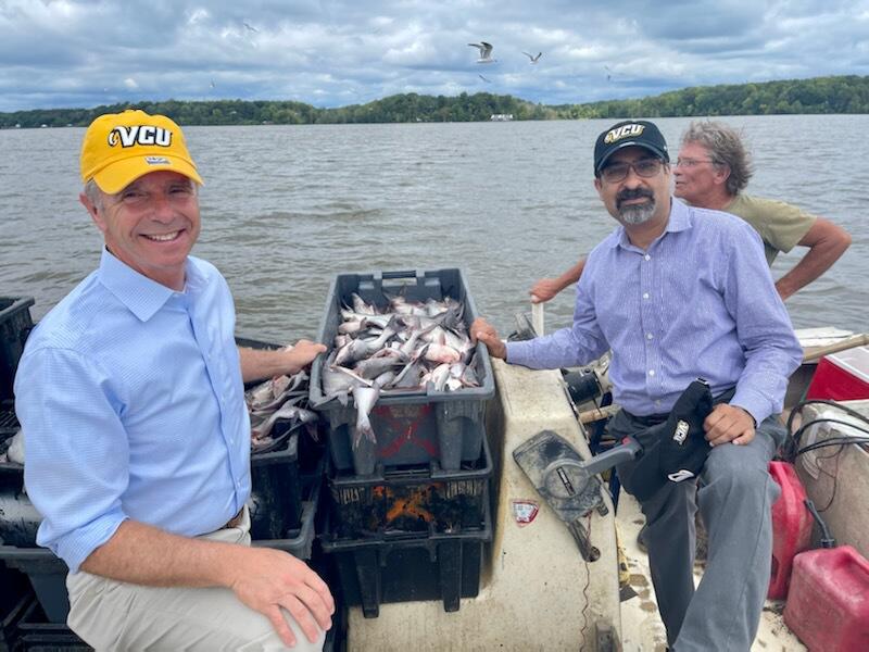 Two men standing on a boat between a container of fish