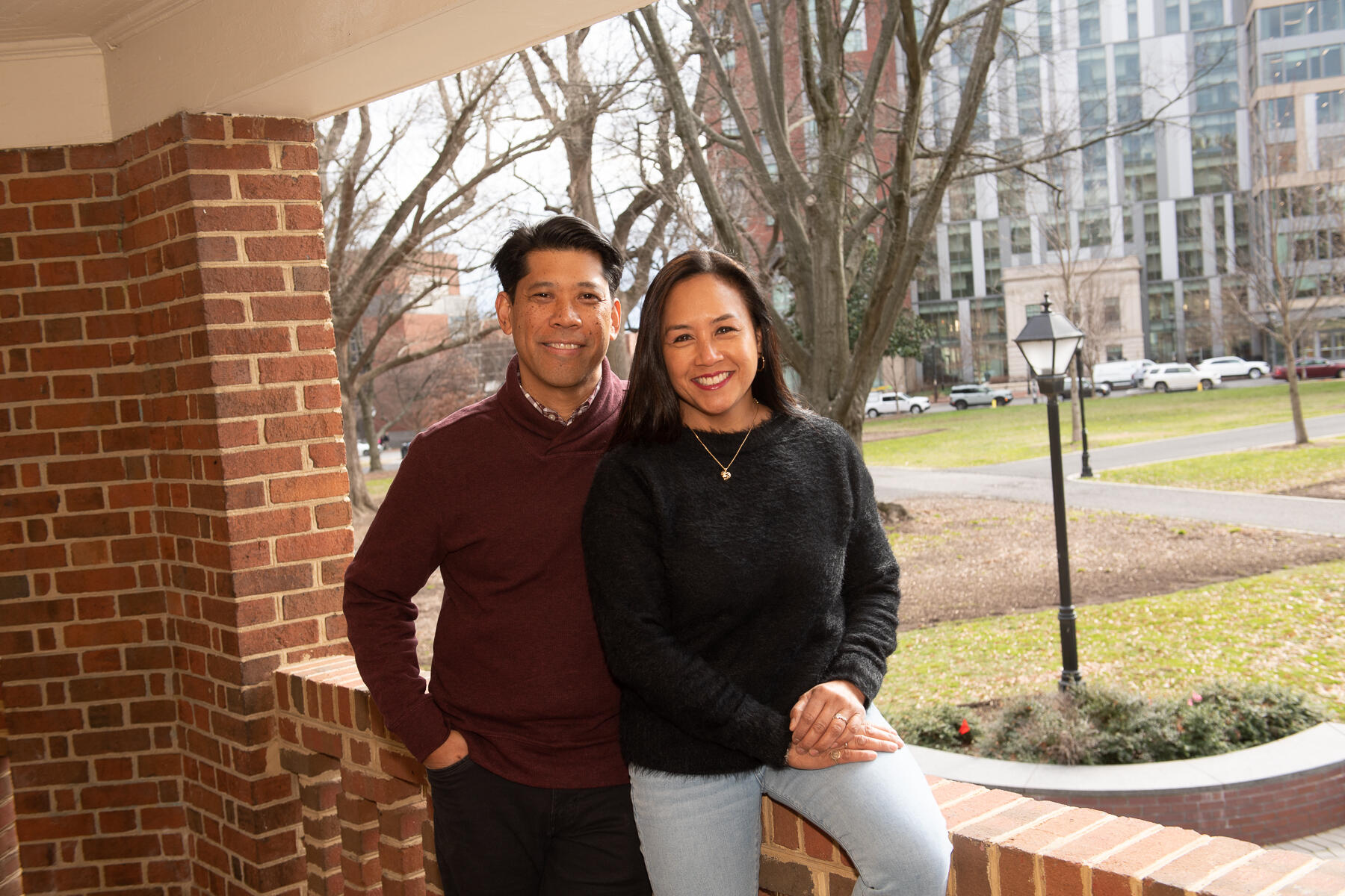 A photo of a man standing behind a woman who is sitting on a brick balcony