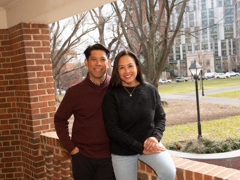 A photo of a man standing behind a woman who is sitting on a brick balcony
