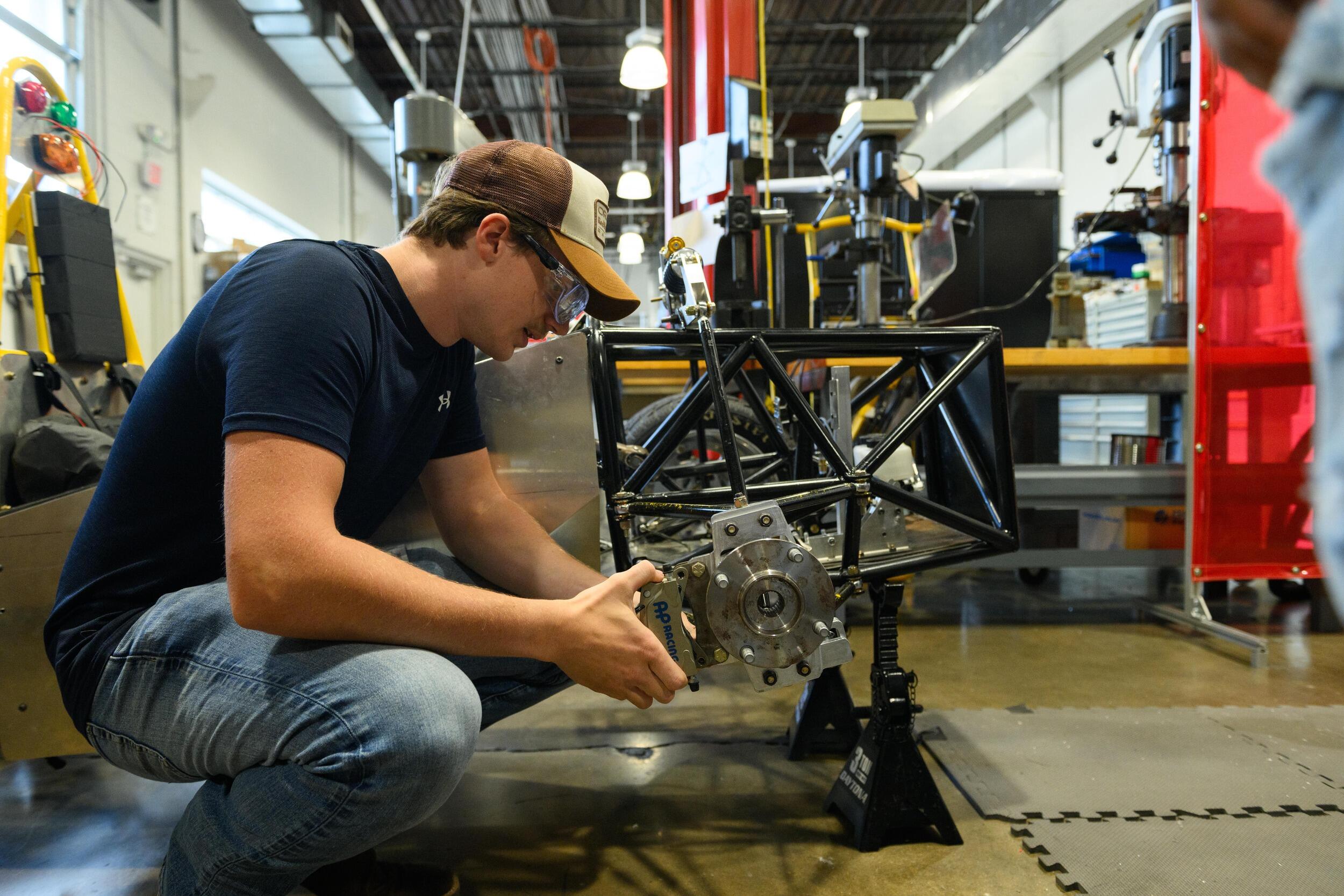A photo ofa man kneeling in front of a mechanical piece. 