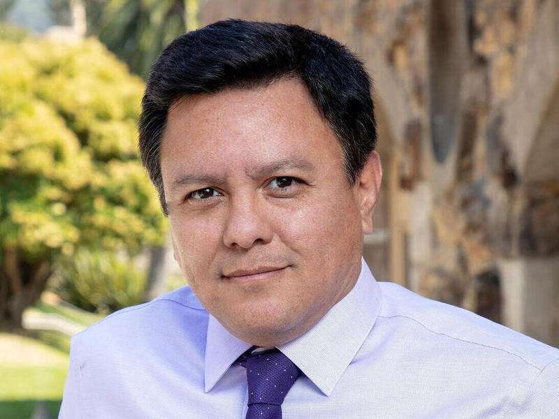 A photo of a man with a light purple button up shirt and a dark purple tie. 