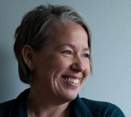 A photo of a woman from the chest up smiling and looking to the left. 