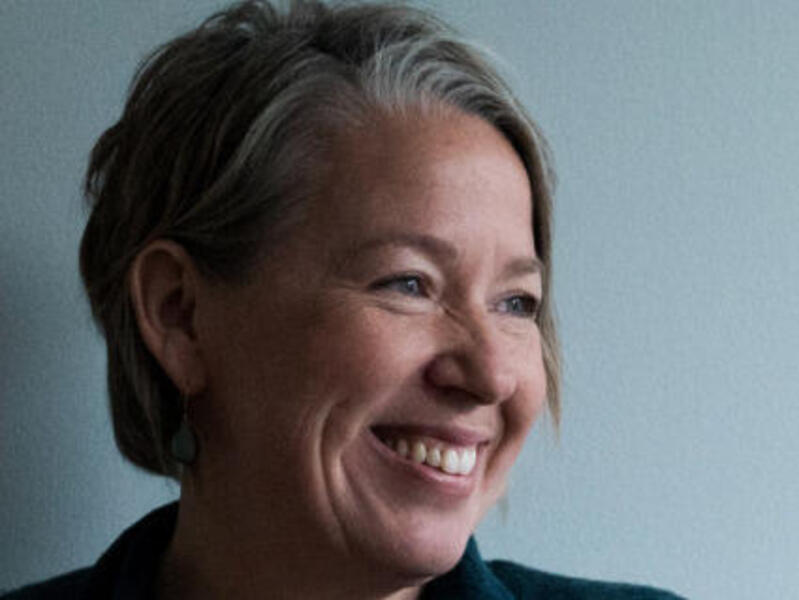 A photo of a woman from the chest up smiling and looking to the left. 