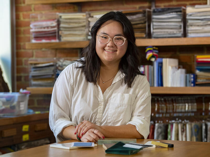 A photo of a woman sitting at a table with notebooks on it. 
