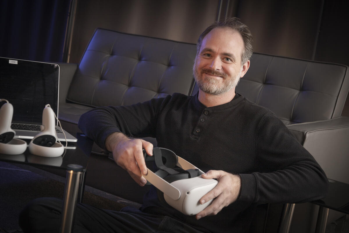 A man wearing a black long sleeve shirt holding a VR headset. 