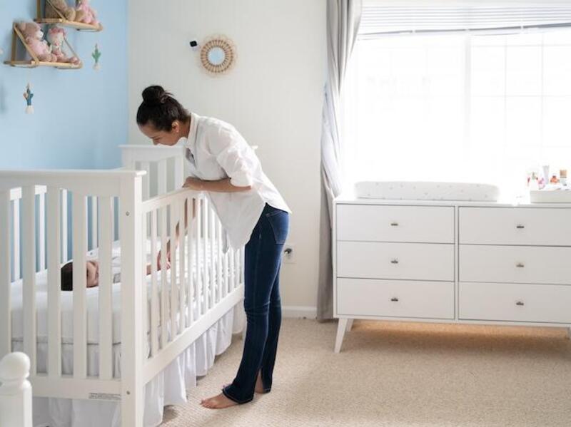 A woman checks on a baby lying down in a crib.