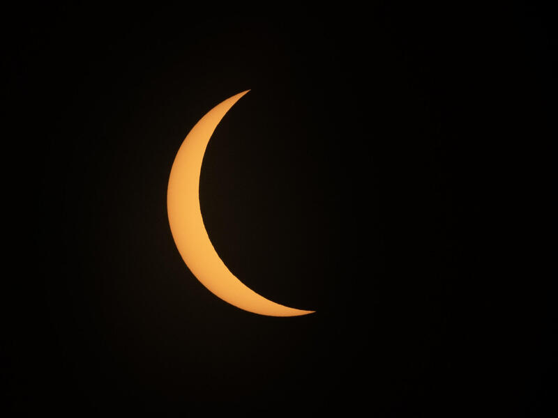 A photo of the sun mostly covered by a round shadow in front of a black sky.