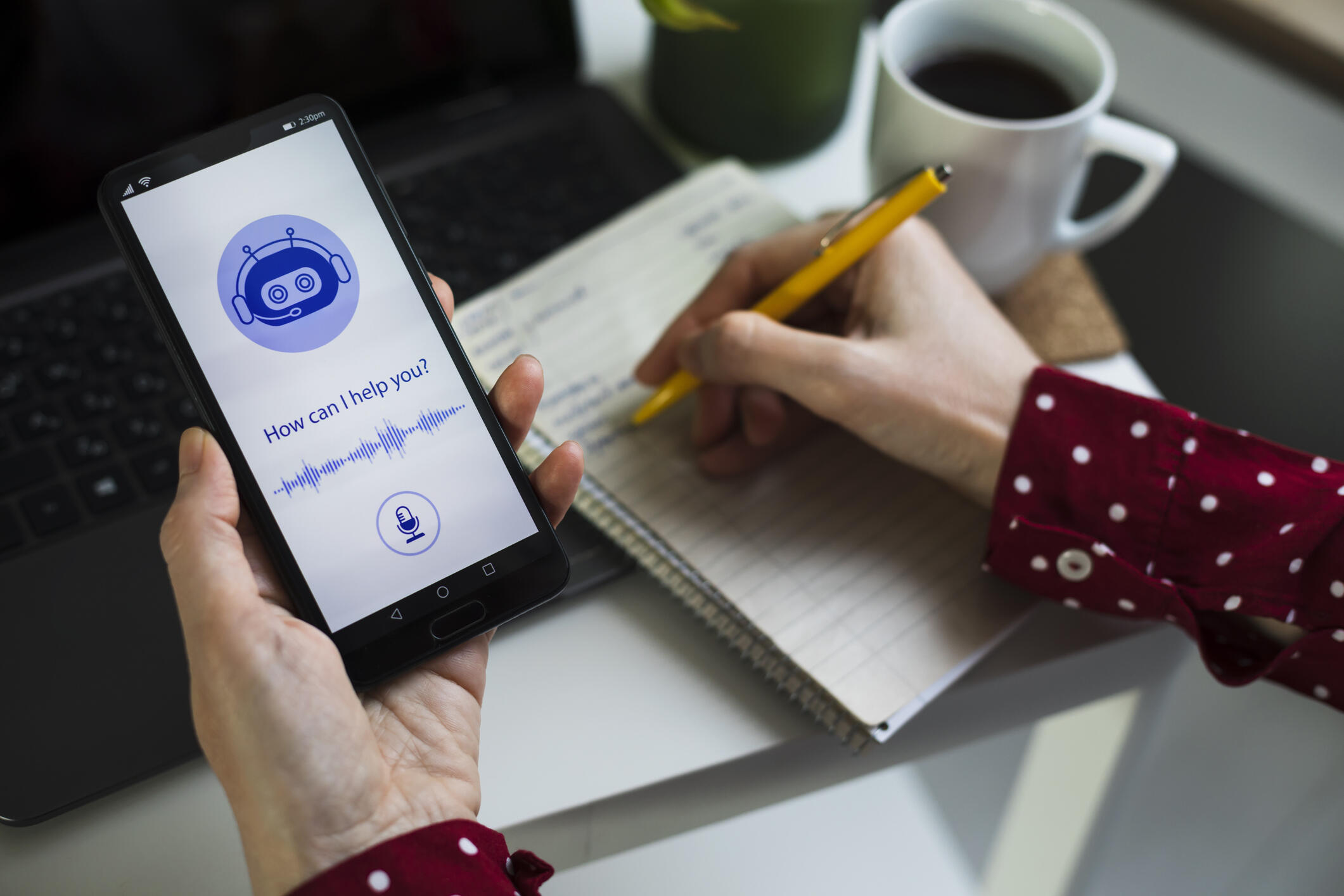 A photo of two hands. One hand is holding a smart phone and the other is holding a pen that is writing 