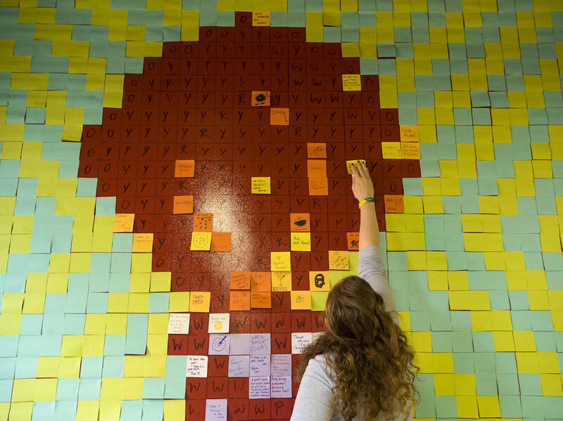 A person applies a sticky note on grid of other similar pieces of paper.
