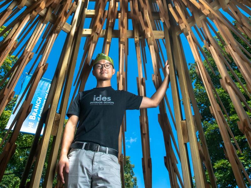 An Liu inside “Helper” the Branch Museum of Architecture. Young man standing inside a wood-frame structure