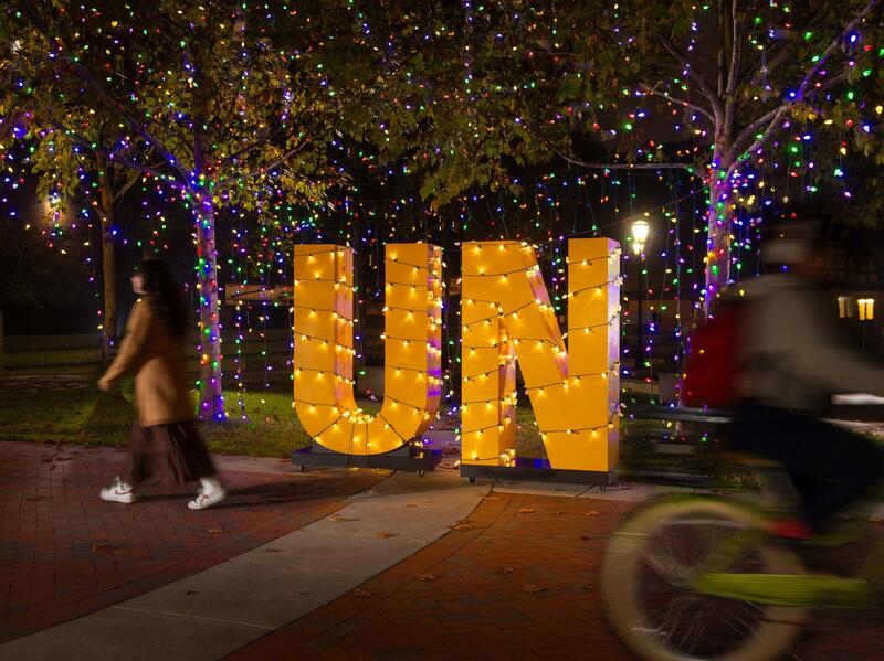 A gold sign of the letters UN is lit by holiday lights at night.