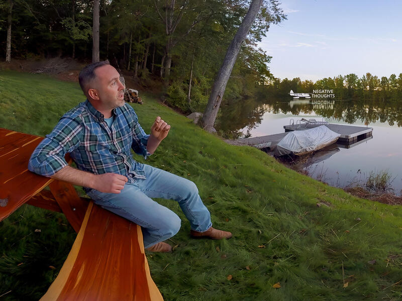 A man sitting on a picnic bench facing a river 