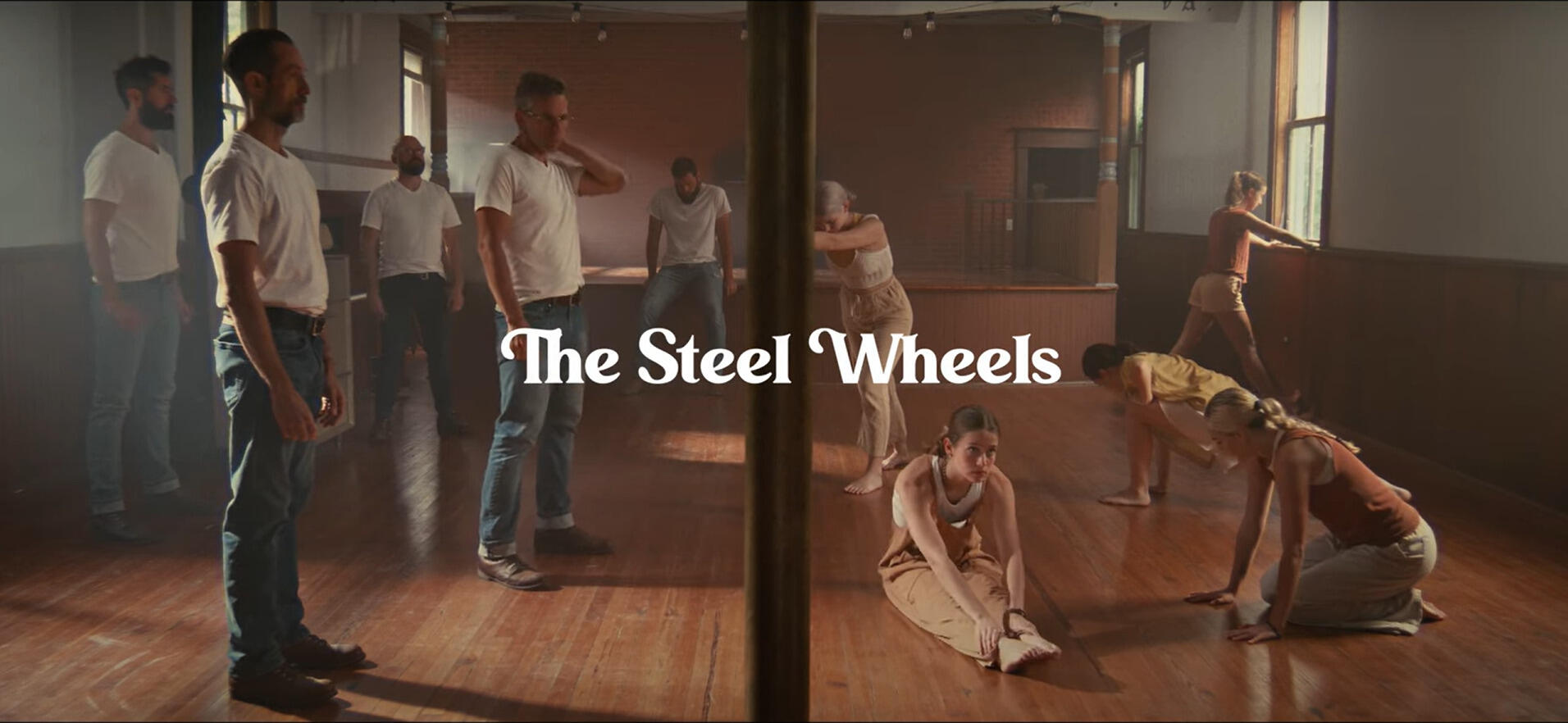 A photo of five men standing on the left side of a room and five young women stretching on the other side of it. 